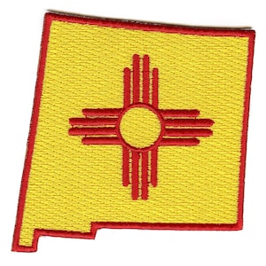 Op de afbeelding: Een gele geborduurde patch in de vorm van de staat New Mexico met een rood Zia-symbool in het midden.
