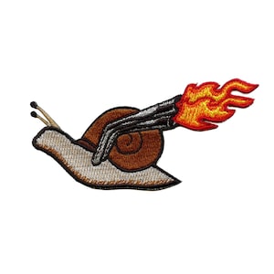 Puede incluir: Un parche bordado de un caracol con un jetpack en la espalda, el jetpack está en llamas. El caracol es marrón y blanco, el jetpack es plateado y el fuego es rojo y amarillo.