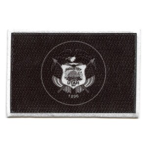 Puede incluir: Parche bordado en blanco y negro con el sello del estado de Utah. El sello representa una colmena, una cordillera, una salida del sol y las palabras "Industry" y "Utah". El año "1896" también está incluido en el sello.