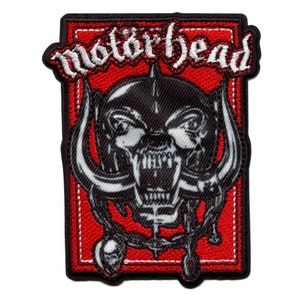 May include: A red and white embroidered patch with the band name "Motorhead" in white lettering and a black and white image of a snarling skull with horns.