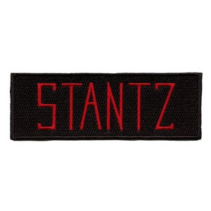 Könnte beinhalten: Schwarzer Stoff-Patch mit dem in Rot gestickten Wort "STANTZ".