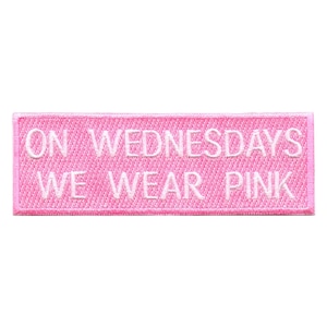 Peut inclure: Patch en tissu rose avec une broderie blanche qui dit "ON WEDNESDAYS WE WEAR PINK".