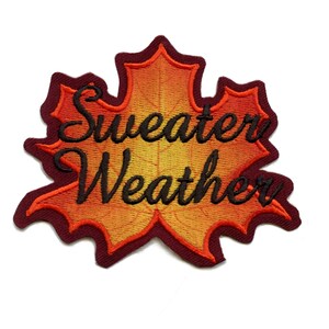 May include: An orange and red embroidered iron-on patch shaped like a maple leaf with the text "Sweater Weather" in black.