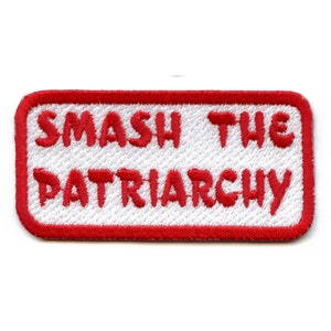 May include: Rectangular patch with the words "SMASH THE PATRIARCHY" embroidered in red on a white background. The patch has a red border and is likely designed to be sewn or ironed onto clothing or accessories.