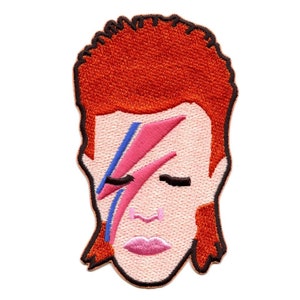 Puede incluir: Parche bordado con una ilustración de dibujos animados de David Bowie con su característico maquillaje de rayo. El parche está en tonos de rojo, rosa, azul y negro.