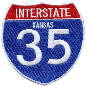 May include: A blue and red Interstate highway sign with the number 35 and the word "Kansas" in white lettering.