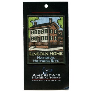Op de afbeelding: Geborduurde patch met het Lincoln Home National Historic Site. De patch toont een bruin huis met witte afwerking, een hek en groene bomen tegen een blauwe lucht. De tekst "LINCOLN HOME NATIONAL HISTORIC SITE" staat eronder.