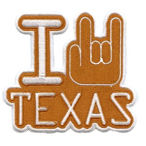 May include: White embroidered patch with the words "I" and "TEXAS" on a brown background. The "I" is followed by a white outline of a hand giving the rock and roll hand gesture.