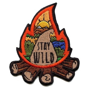 Può includere: Toppa ricamata da stirare con un design a forma di falò. Le fiamme sono arancioni e rosse, e il falò è fatto di tronchi marroni. Il centro della toppa presenta una roccia color sabbia con le parole "Stay Wild" in testo nero. La roccia è circondata da alberi verdi e un lago blu.