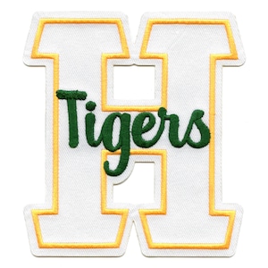 Może przedstawiać: Biała łatka z filcu z żółtym obramowaniem litery H. Słowo "Tigers" jest napisane zielonym kursywą wewnątrz litery.