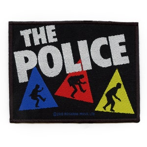 May include: Black fabric patch with white text that reads "THE POLICE" with three stylised figures in blue, red and yellow triangles. The text "©2018 ROXANNE MUSIC LTD" is at the bottom.