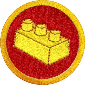 Könnte beinhalten: Ein gelber gestickter LEGO-Stein-Patch mit rotem Hintergrund und goldener Umrandung.
