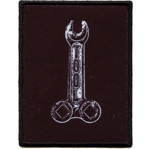 Puede incluir: Un parche de tela negro con un diseño de llave inglesa blanca. La llave inglesa tiene la palabra "TOOL" escrita en ella.