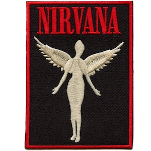 May include: Embroidered patch with the word "NIRVANA" in red above a cream-coloured angel figure with outstretched arms and wings. The patch has a black background with a red border.