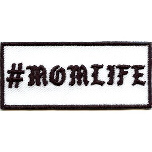 Puede incluir: Parche blanco bordado con costuras negras y el texto "#MOMLIFE" en una fuente estilizada.