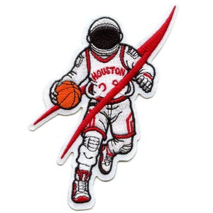 Puede incluir: Un parche bordado con un astronauta de dibujos animados que lleva una camiseta de baloncesto roja y blanca con la palabra "HOUSTON" en la parte delantera. El astronauta está botando un balón de baloncesto y volando por el espacio, representado por una línea diagonal roja.