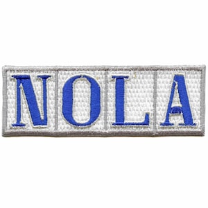 May include: A white embroidered patch with the word "NOLA" in blue lettering.