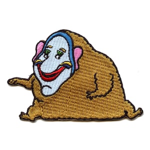 May include: Embroidered patch featuring a cartoon character with a brown furry body, a white face with a red smile, blue and yellow eyes, and a pink and blue hat.