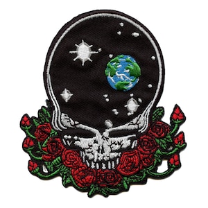 Puede incluir: Un parche bordado con una calavera en blanco y negro con una tierra azul y verde en su interior. La calavera está rodeada de rosas rojas con hojas verdes.