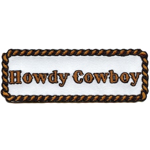 Può includere: Una toppa ricamata bianca con un bordo di corda marrone. Il testo "Howdy Cowboy" è ricamato in marrone sulla toppa.