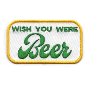 May include: A white rectangular patch with a yellow border. The patch has green embroidered text that reads "Wish You Were Beer".