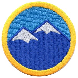 以下が含まれることがあります： 青い背景に白い刺繍の山が施された、黄色の縁取りのある丸いパッチ。