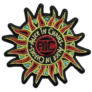 Puede incluir: Un parche bordado negro, rojo y amarillo con un diseño de sol radiante. El centro del parche presenta un círculo con el texto "Alice in Chains" y las iniciales del grupo "AIC" en rojo.