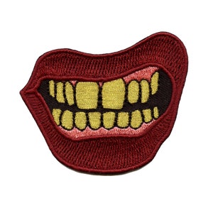 Può includere: Una toppa ricamata rossa con un grande set di denti d'oro. I denti sono contornati di nero e le labbra sono di un rosso più scuro.