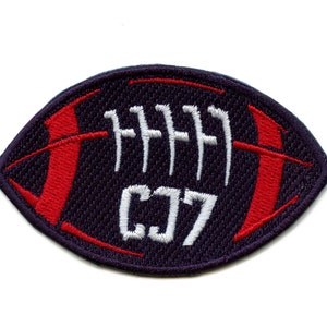 May include: A navy blue embroidered patch shaped like a football with red stitching and white laces. The text "CJ7" is embroidered in white on the patch.