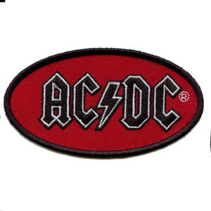 May include: Red oval-shaped patch with the band name "AC/DC" in black with a silver outline and a lightning bolt in the middle.