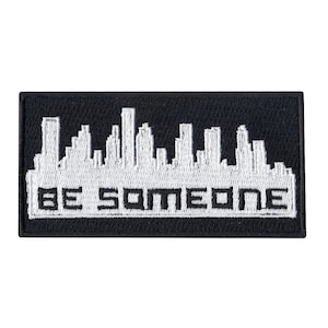May include: Black and white embroidered patch with a cityscape silhouette and the text "BE SOMEONE" in white.