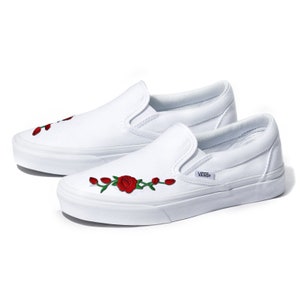 May include: White canvas slip-on Vans shoes with red rose embroidery.