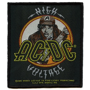 Puede incluir: Parche bordado negro con un círculo amarillo y naranja que contiene el texto "High Voltage" y el nombre de la banda "AC/DC" en amarillo. Una imagen de dibujos animados de un hombre con una gorra de béisbol y una guitarra está en el centro del círculo.