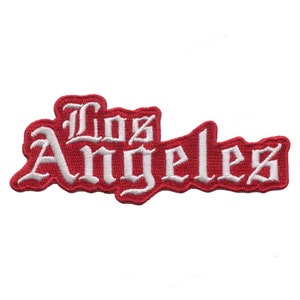 Pode incluir: Etiqueta bordada vermelha com letras brancas que dizem "Los Angeles" em uma fonte estilizada.