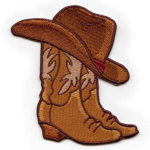 Puede incluir: Botas de vaquero marrones y un sombrero de vaquero marrón con una banda roja. Las botas y el sombrero están bordados con costuras.