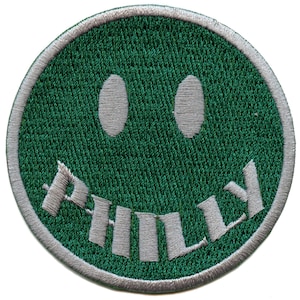 May include: Green embroidered patch with a smiling face and the word "Philly" written in a white arc below the face.