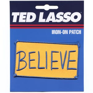 May include: A yellow iron-on patch with blue stitching that says "BELIEVE" in a handwritten style. The patch is packaged on a blue card with the words "Ted Lasso" and "Iron-On Patch" printed on it.