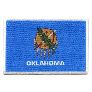 May include: A blue fabric patch with a white border. The patch features the state seal of Oklahoma, which depicts an indigenous American holding a spear and shield. The text "OKLAHOMA" is printed in white below the seal.