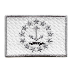 May include: A white embroidered patch with a gray anchor and a circle of thirteen stars. The anchor is centered in the circle of stars. The patch has a gray border.