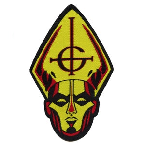 Puede incluir: Parche bordado amarillo y rojo con una imagen en blanco y negro de una cara que lleva una mitra con un símbolo de cruz y círculo.