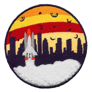 May include: A white space shuttle with orange flames launching into a yellow, orange, and red sunset over a dark blue cityscape. The shuttle is surrounded by white clouds.
