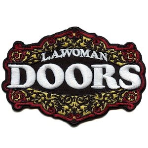 May include: A black embroidered patch with a gold and red ornate frame. The text "LA WOMAN DOORS" is in white embroidery.