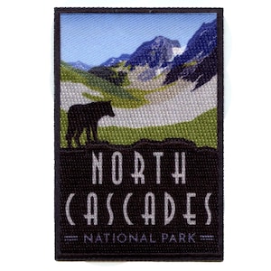 May include: A black and white embroidered patch with a silhouette of a wolf in front of a mountain range. The text "NORTH CASCADES NATIONAL PARK" is printed in white on a black background.