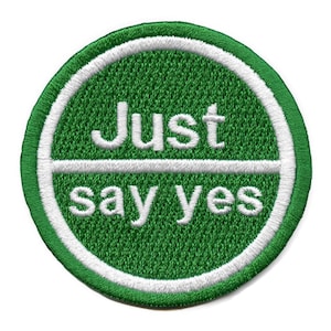 May include: A green and white circular embroidered patch with the text "Just say yes" in white.