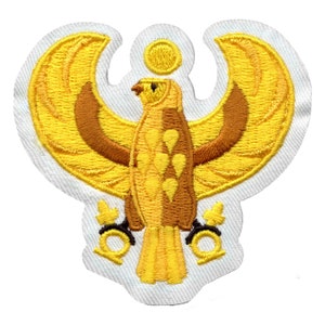 May include: A yellow and brown embroidered patch depicting a stylized eagle with outstretched wings. The eagle is holding a sun in its beak and has two golden rings at its feet.