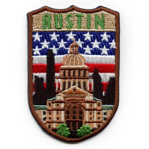 May include: Embroidered patch with a brown shield shape. The shield features a depiction of the Texas State Capitol building in Austin, Texas. The building is brown and beige with a white dome. The building is set against a background of an American flag with red, white, and blue stripes and white stars. The words "AUSTIN" are embroidered in green above the building.