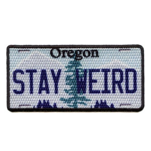 Puede incluir: Un parche bordado azul y blanco con el texto "Oregon" y "STAY WEIRD" sobre un fondo blanco. El parche tiene un borde negro.