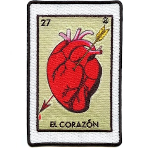 May include: A vintage-style embroidered patch featuring a red heart pierced by an arrow. The heart is surrounded by a beige background with the text "EL CORAZÓN" and the number "27" in black. The patch has a white border with a black outline.
