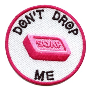 May include: A white circular embroidered patch with a pink bar of soap and the text "Don't Drop Me" in black.