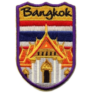 Puede incluir: Un parche bordado con un borde morado, que presenta un edificio dorado y naranja con un techo rojo, y el texto "Bangkok" en letras negras. El edificio está sobre un fondo de la bandera tailandesa.